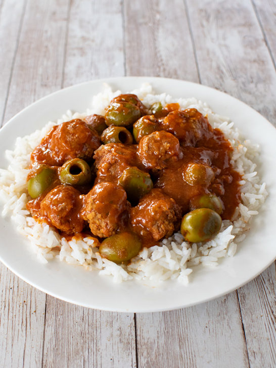 Moroccan-Israeli Meatballs and Olives over white rice on a white plate on a white wood table