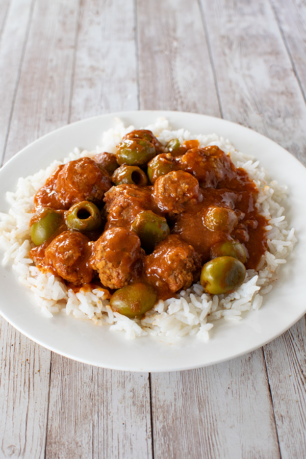 Moroccan-Israeli Meatballs and Olives over white rice on a white plate on a white wood table