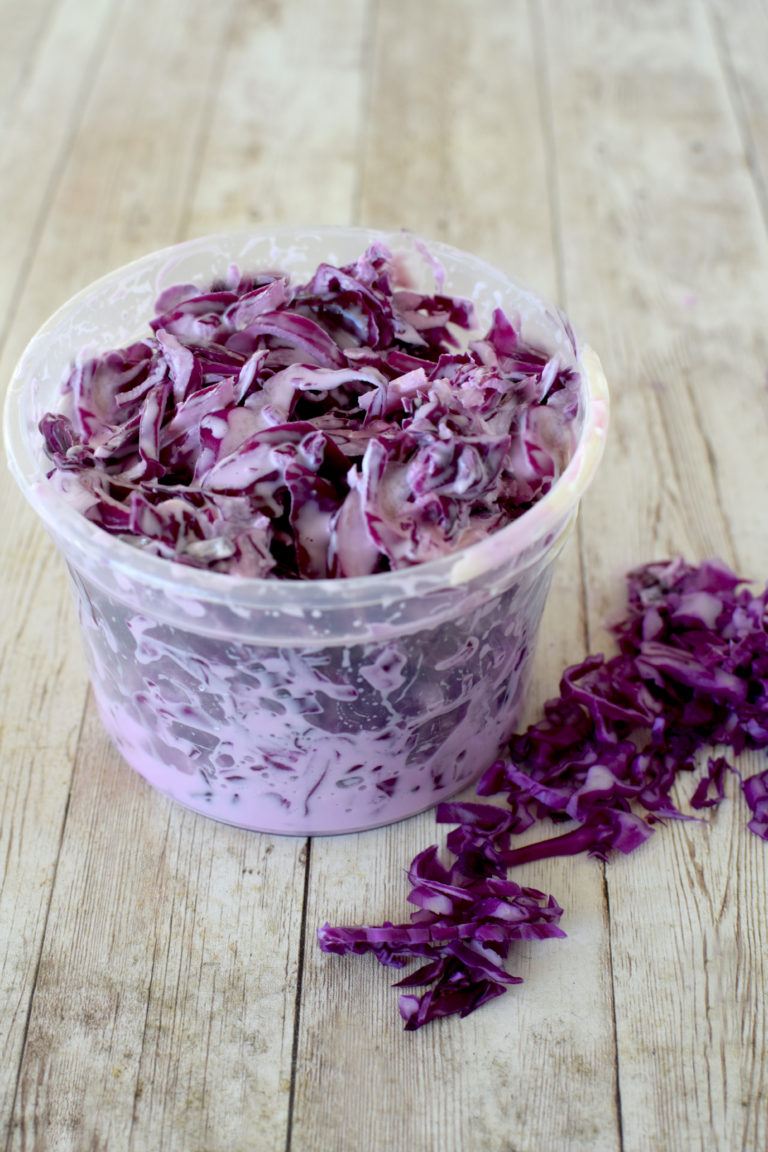 Israeli Red Cabbage Salad in a clear deli container on a white wood table