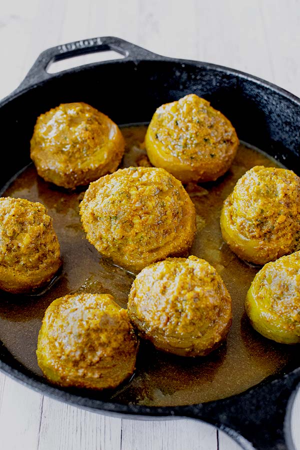 8 artichoke bottoms stuffed with ground beef in a gravy of cumin and turmeric in a cast iron pan.