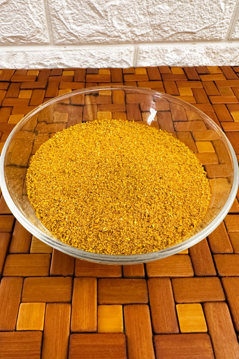 homemade shawarma seasoning in a glass bowl on a wooden mat with a white brick background