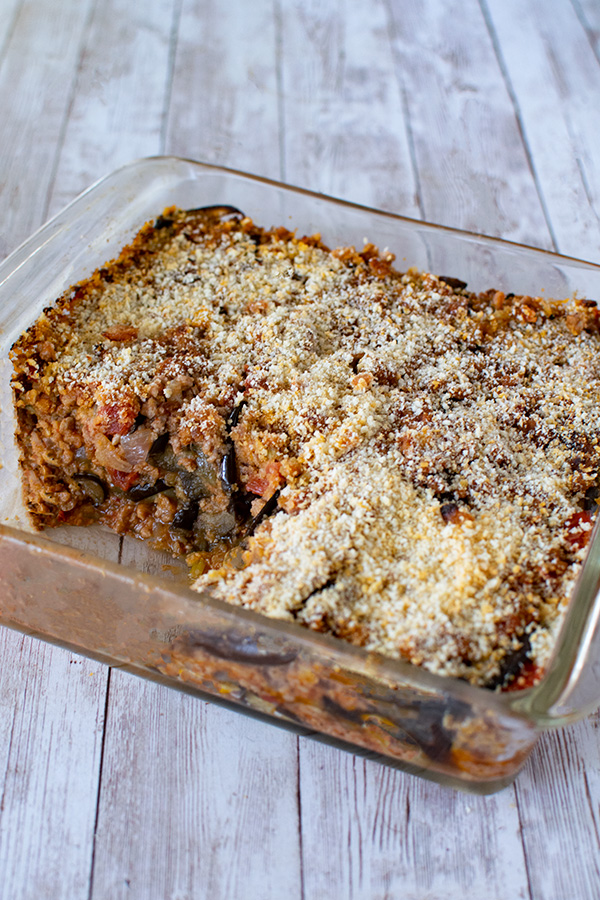 Moussaka in a glass dish topped with breadcrumbs and a piece missing