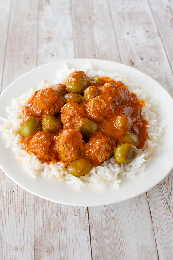 meatballs and olives over rice on a white plate