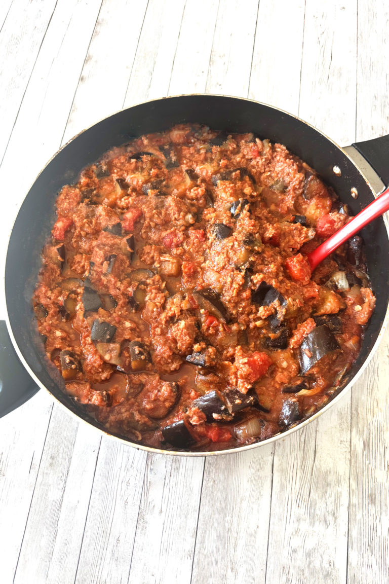 Turkish-style moussaka in a pan with a red serving spoon on a white wood table