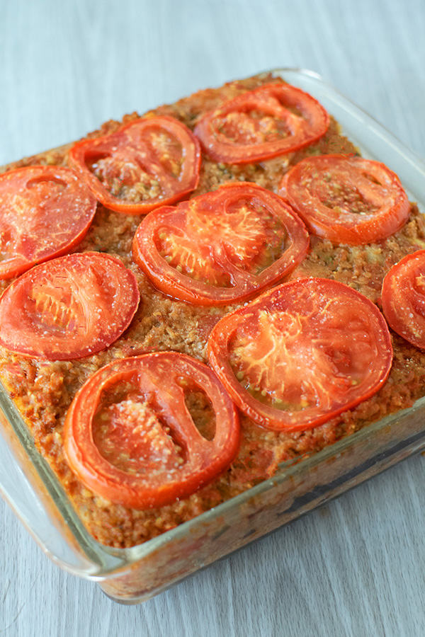 Israeli Style Moussaka with ground beef covered with tomato slices in a clear square baking dish