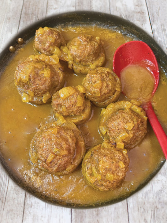 Cooked Israeli-style stuffed artichokes with sauce in a pan with a red spoon on a white wood table