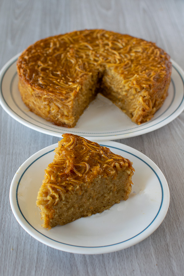 A round Jerusalem Kugel on a white plate with a slice on another white plate on a white wood table background 