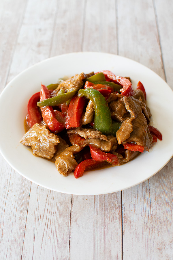 Kosher pepper steak on a white plate on a white wood table