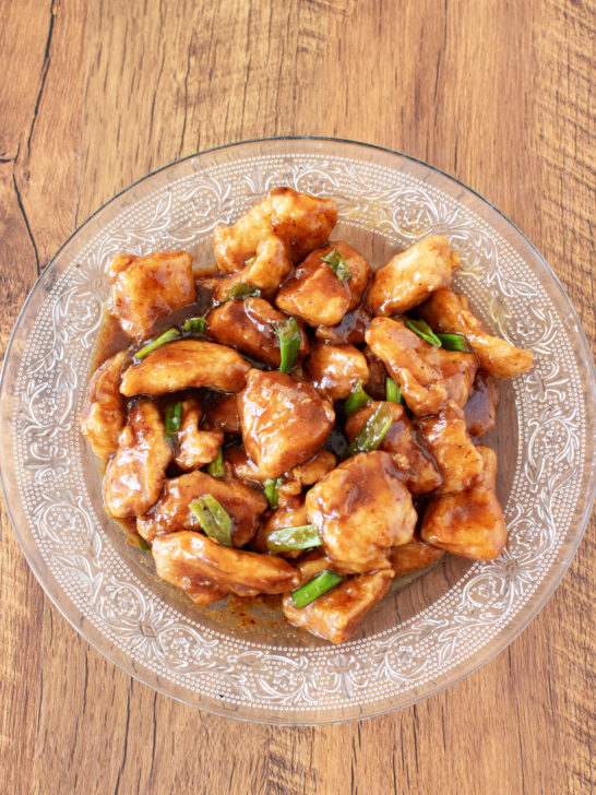 Kosher Mongolian chicken in a clear bowl on a dark wood table.