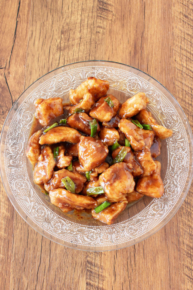 Kosher Mongolian chicken in a clear bowl on a dark wood table.
