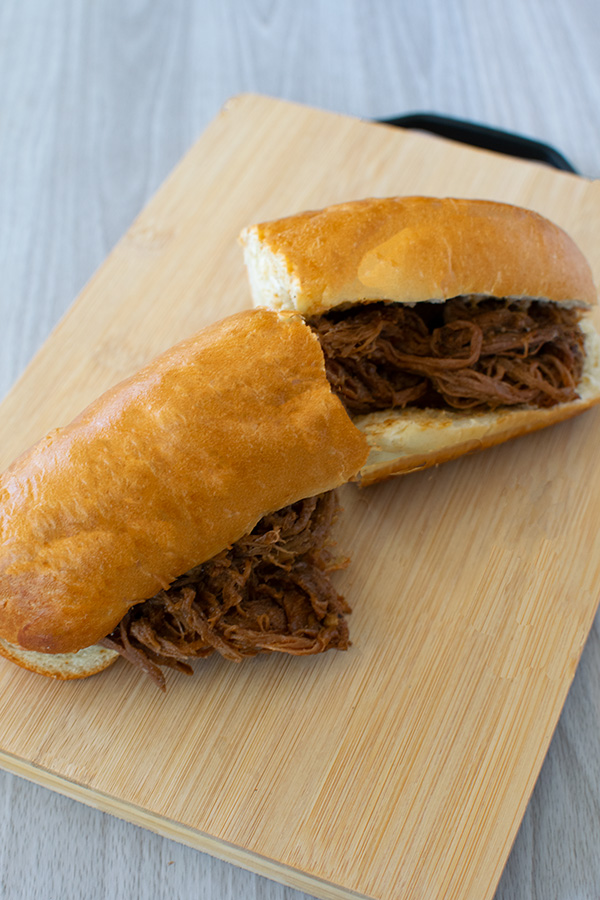 Pulled beef sandwich, cut in two, on wooden cutting board on white wood background