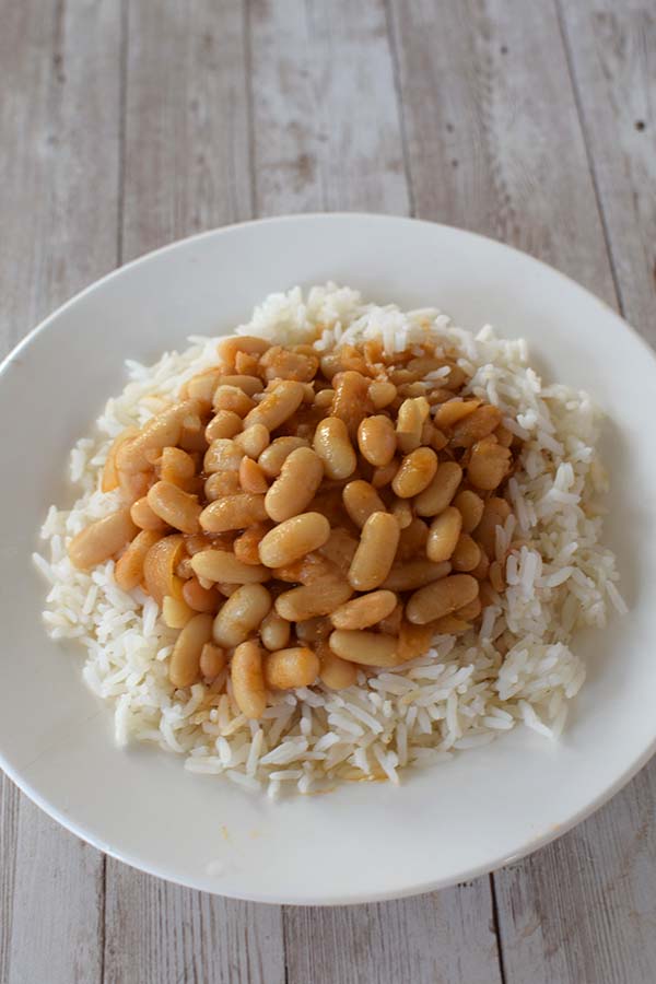 Israeli bean soup on rice on a white plate on a white wood table