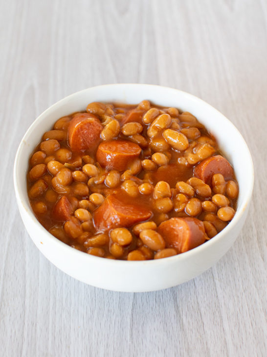 Franks and beans in a white bowl on a white wood table