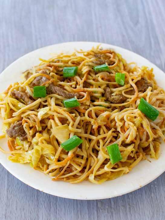 Beef Chow Mein topped with pieces of green onion on a white plate on a white table