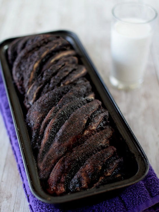 dairy free chocolate babka cake in a pan on a white table with a clear glass of milk nearby