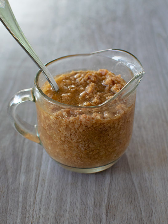 Hamburger gravy in a clear gravy server with a spoon on a white table