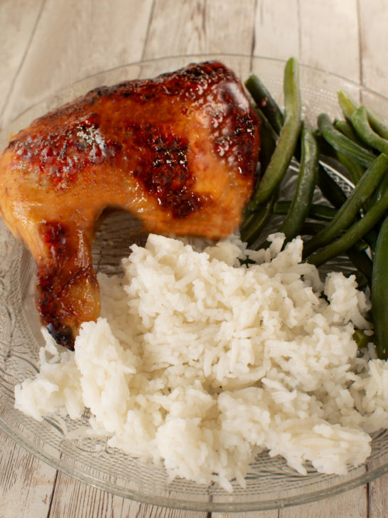 Duck Sauce Chicken leg on a clear plate with rice and green beans on a white wooden table