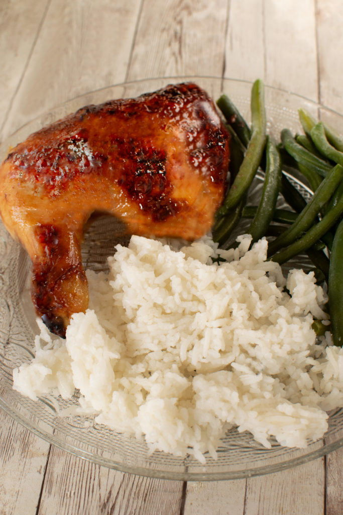 Duck Sauce Chicken leg on a clear plate with rice and green beans on a white wooden table