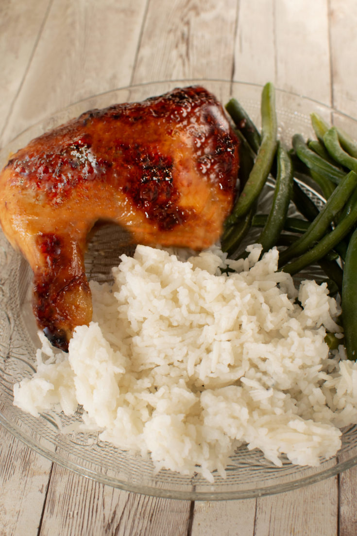 Duck Sauce Chicken leg on a clear plate with rice and green beans on a white wooden table