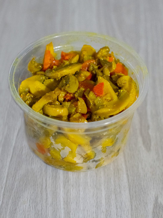 Israeli Mushroom Salad in a clear plastic tub on a white wood table.