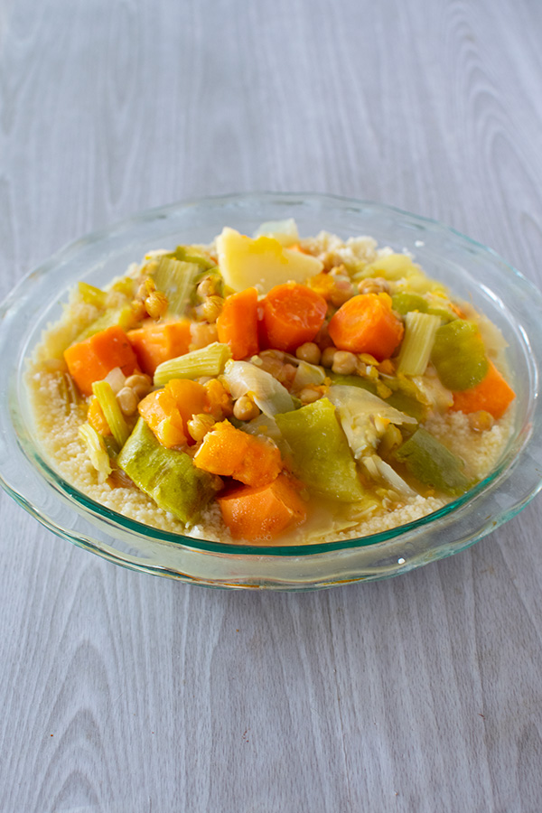 Israeli Vegetable soup on couscous in a clear bowl on a white wood table