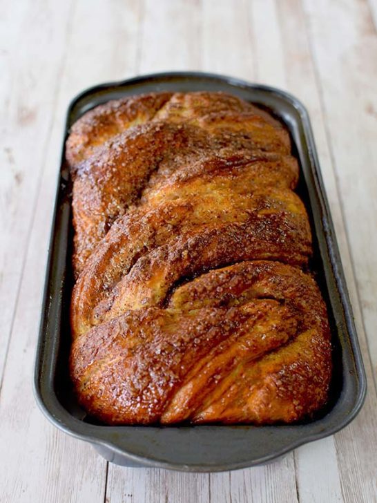 Dairy Free Cinnamon babka in a loaf pan on a white wood table with a clear glass of milk nearby