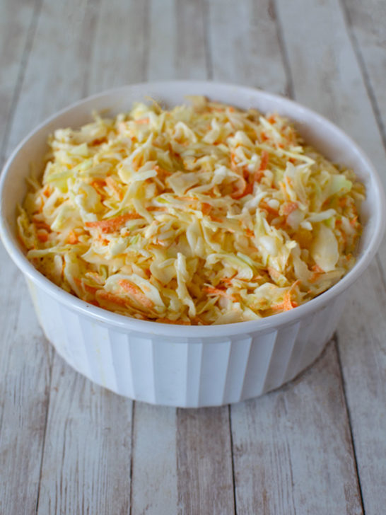 Sweet Deli Cole slaw with shredded cabbage and carrots in a white bowl on a wood background