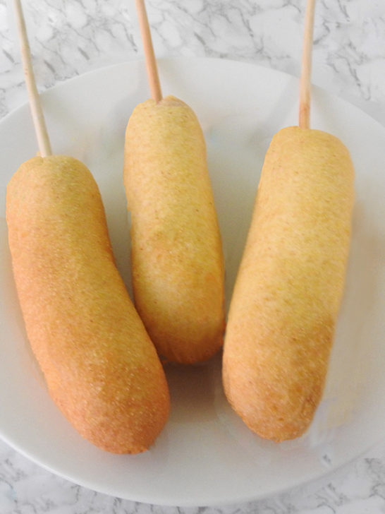 Three corndogs on a white plate.