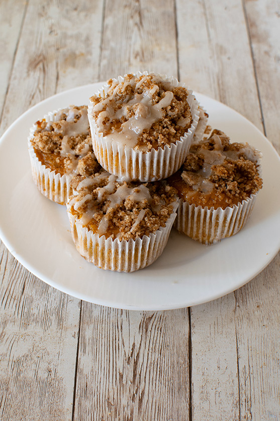 Moist, dairy-free honey muffens for Rosh Hashana with streussel and glaze on a white plate on a white wood talbe.