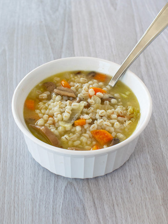 Vegetarian Mushroom Barley Soup in a white bowl with a spoon on a white wood background