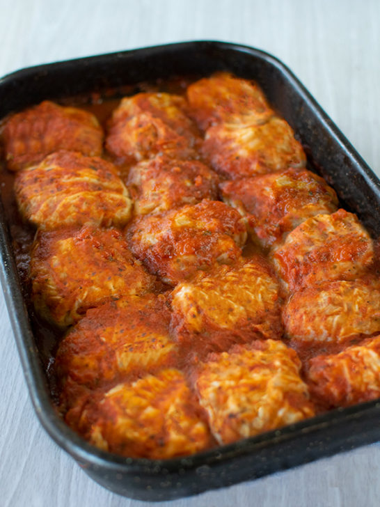 5 rows of stuffed cabbage on a black pan on a white wood table