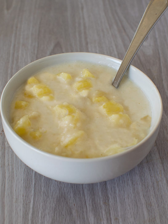 Creamy potato soup in a white bowl with a spoon on a white table