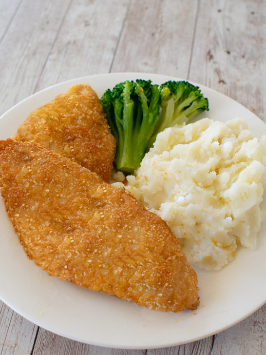 2 pieces of Fried potato flake fish on a white plate with mashed potatoes and broccoli