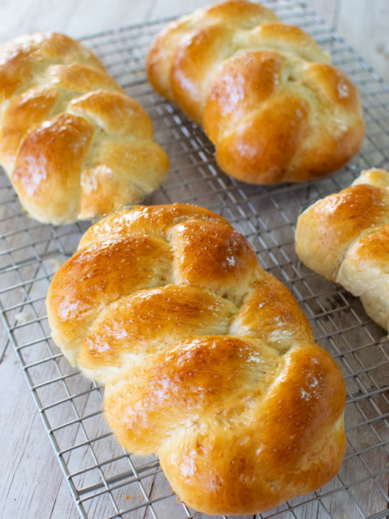 Fluffy challah Rolls on a drying rack on a white wood table
