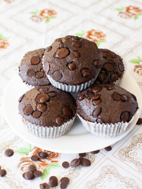 dairy-free chocolate muffins on a white plate on a flowered table with chocolate chips nearby