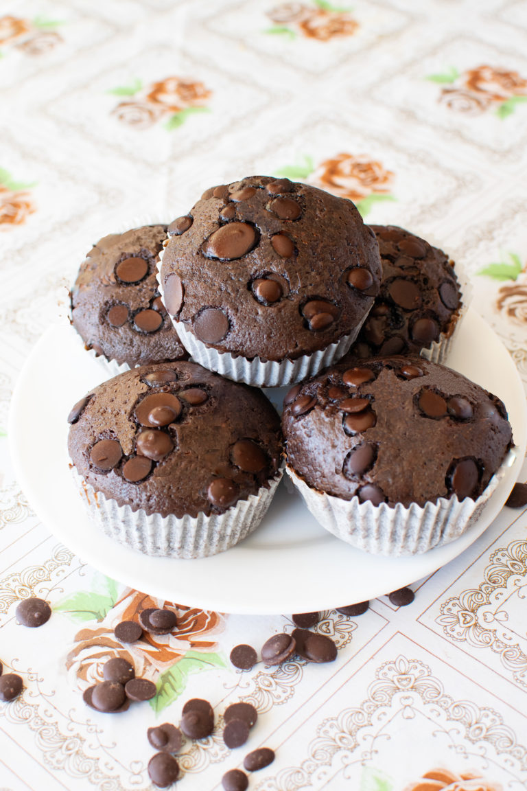 dairy-free chocolate muffins on a white plate on a flowered table with chocolate chips nearby