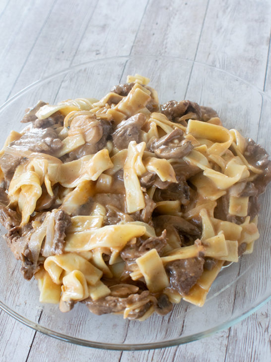 Creamy dairy free beef stroganoff made with long flat noodles served on a clear plate.