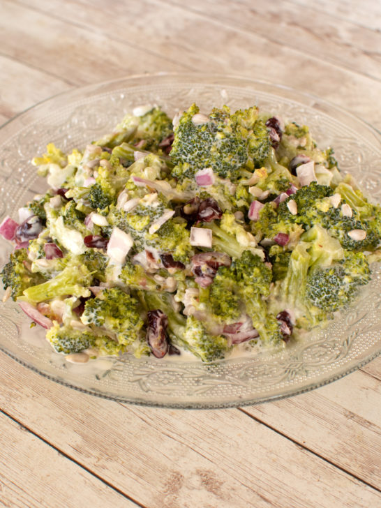 Broccoli salad on a clear plate on a white wood table