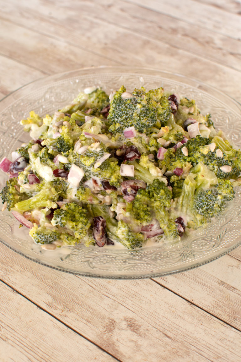 Broccoli salad on a clear plate on a white wood table