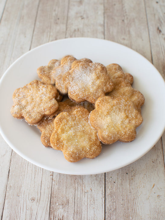 A pile of sugar cookies on a white plate on a white wood table