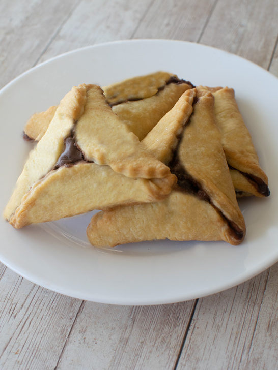Several Hamentaschen on a white plate on a white wood table