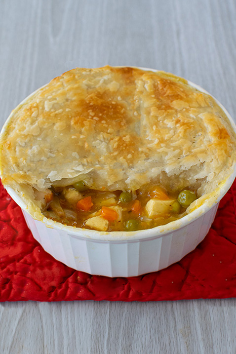 Creamy pot pie with tofu in a single-serve ramekin mostly covered in crispy pastry dough.