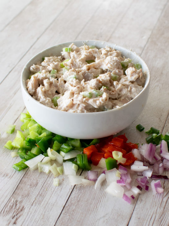 chicken salad turkey salad in a white bowl on a white wood table with vegetables in front