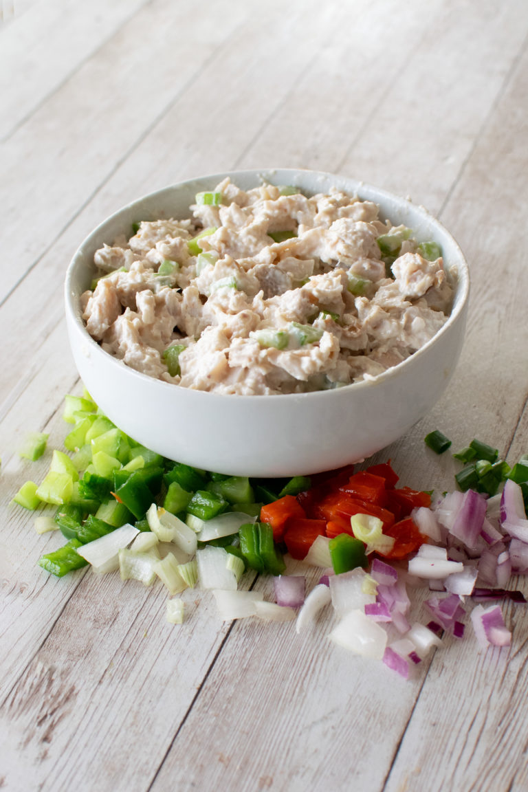 Chicken Salad in a white bowl on a white wood table with vegetables in front
