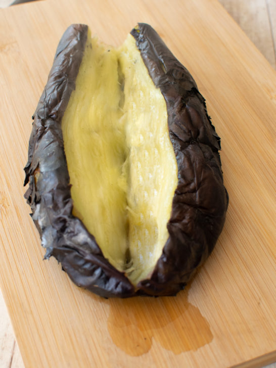 Open roasted eggplant on a wooden cutting board
