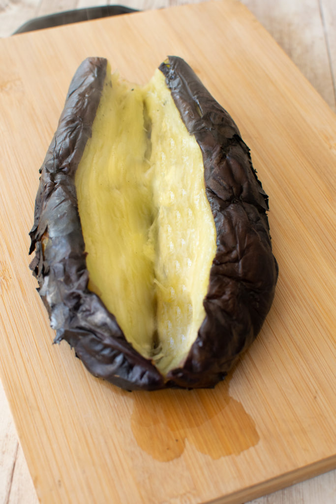 Open roasted eggplant on a wooden cutting board
