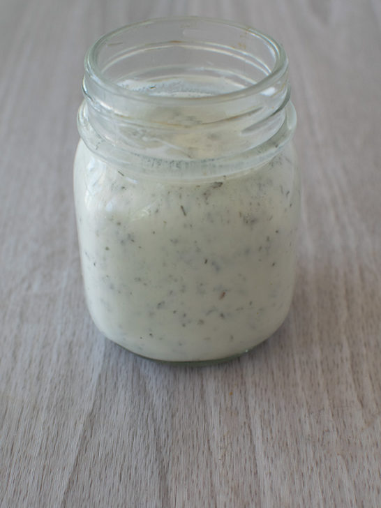 Ranch dressing in a clear jar on a a white table