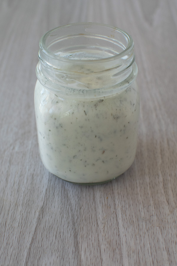 Ranch dressing in a clear jar on a a white table