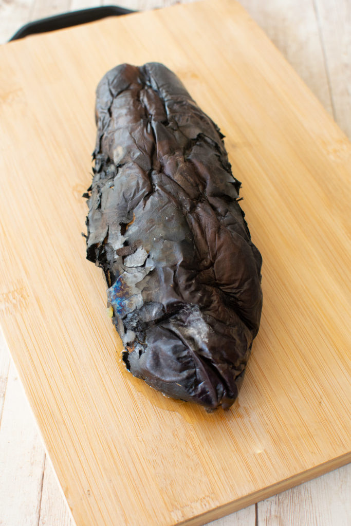 Well roasted whole eggplant on a wooden cutting board