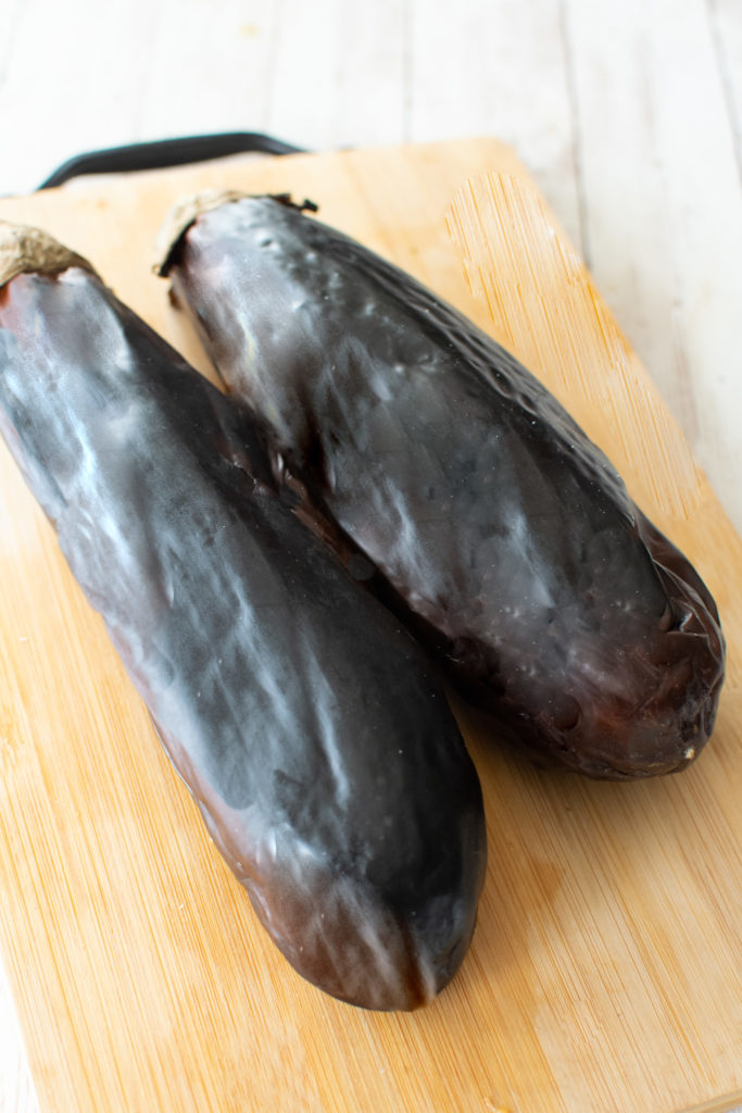 Two whole roasted eggplant on a wooden cutting board